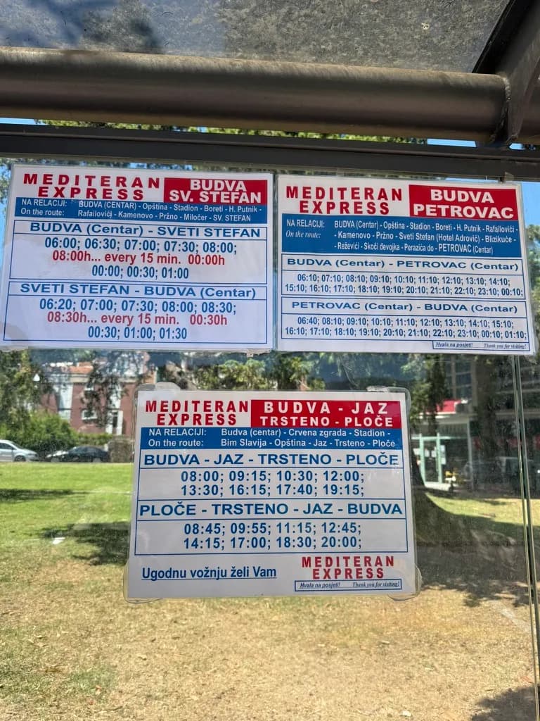 Mediteran Express timetables taped up inside a bus stop shelter in Budva: white sheets with red and blue lettering, one for each route.